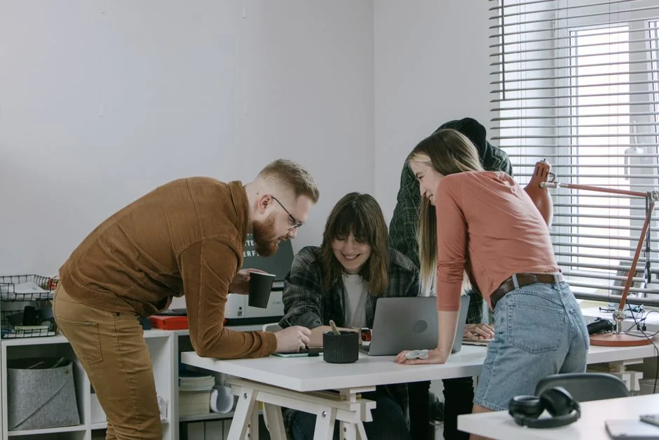 Enseignant utilisant un ordinateur portable pour une leçon virtuelle avec une étudiante affichée à l’écran dans un environnement de classe.
